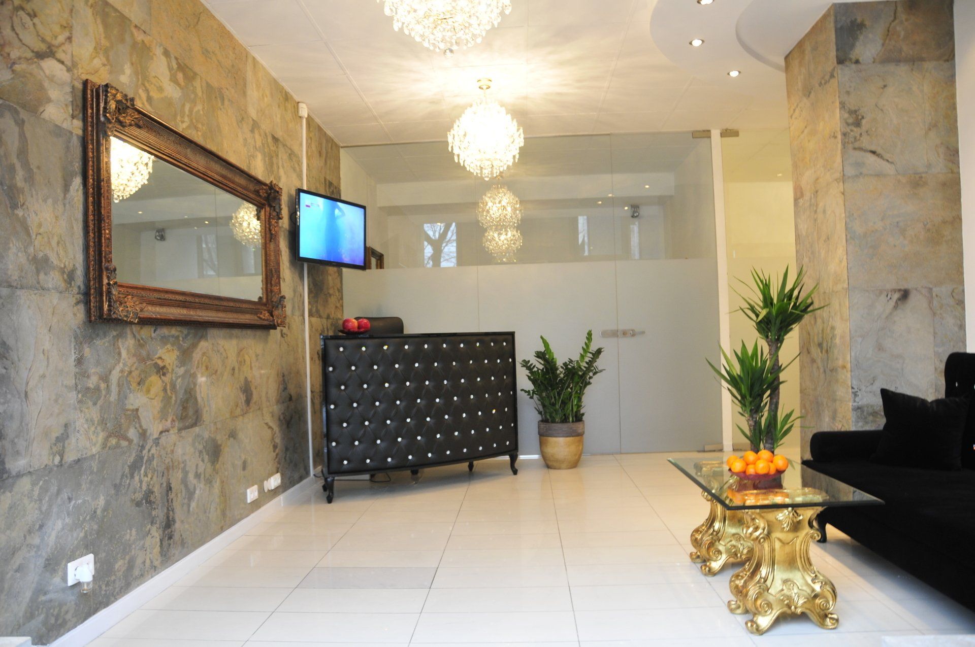Reception area with textured stone walls, large mirror, black tufted desk, and crystal chandeliers.