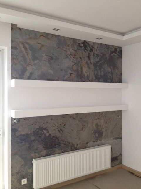 Wall with stone-like texture, two white shelves, a radiator, and recessed lights in the ceiling.