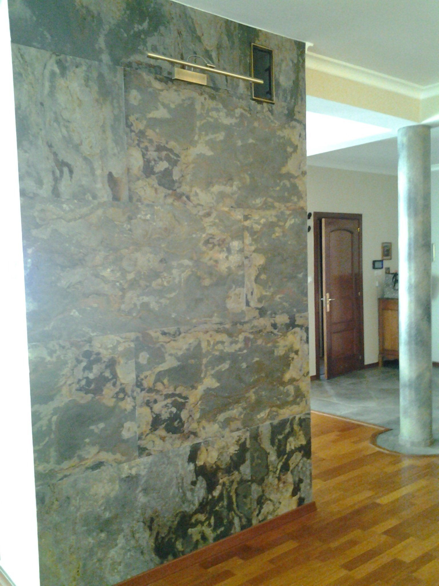 Textured stone wall with gold accent, near a wooden floor and interior doorway.