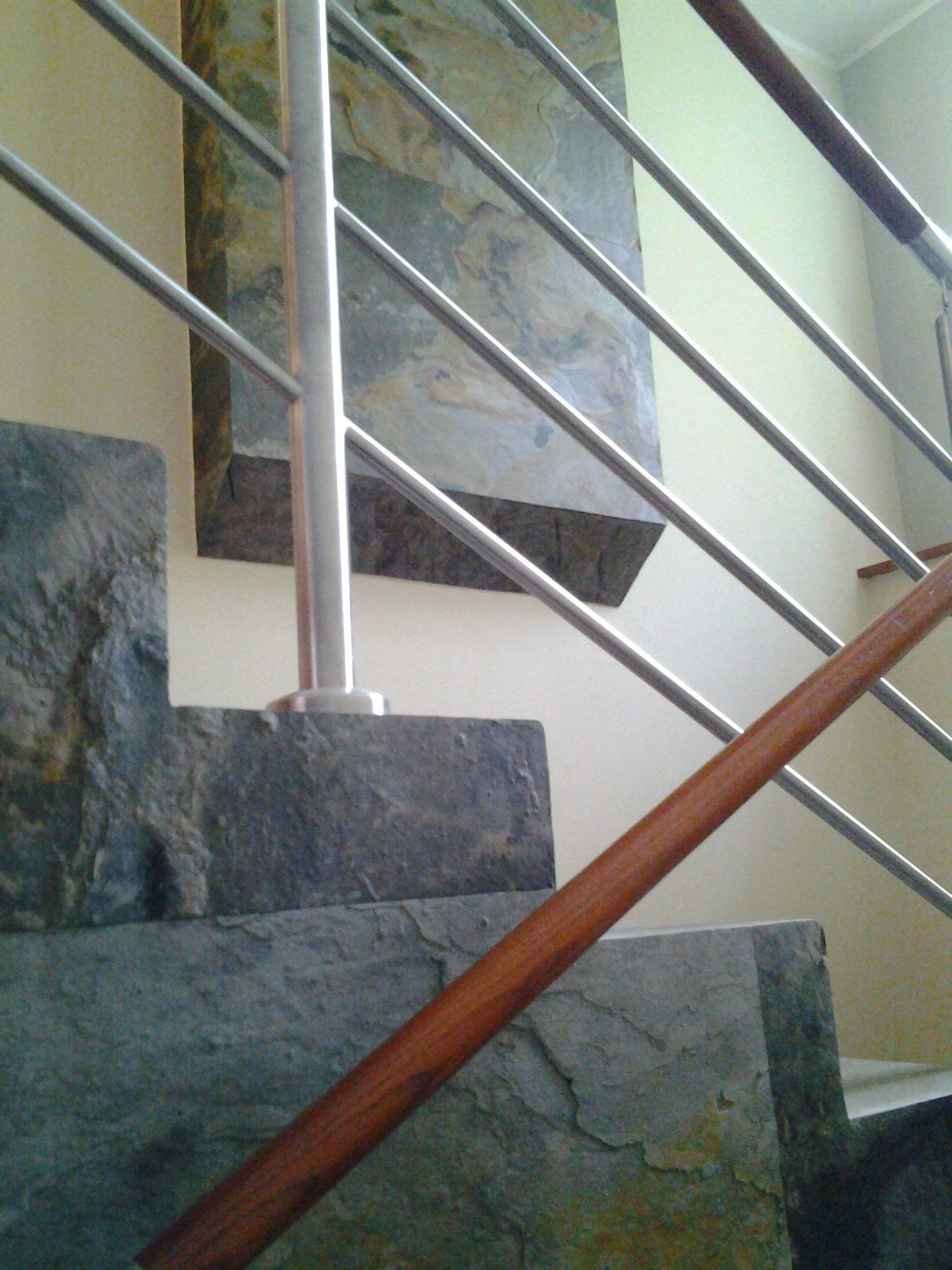 Stone steps with metal and wood railing. A large stone slab is mounted on the wall behind the steps.