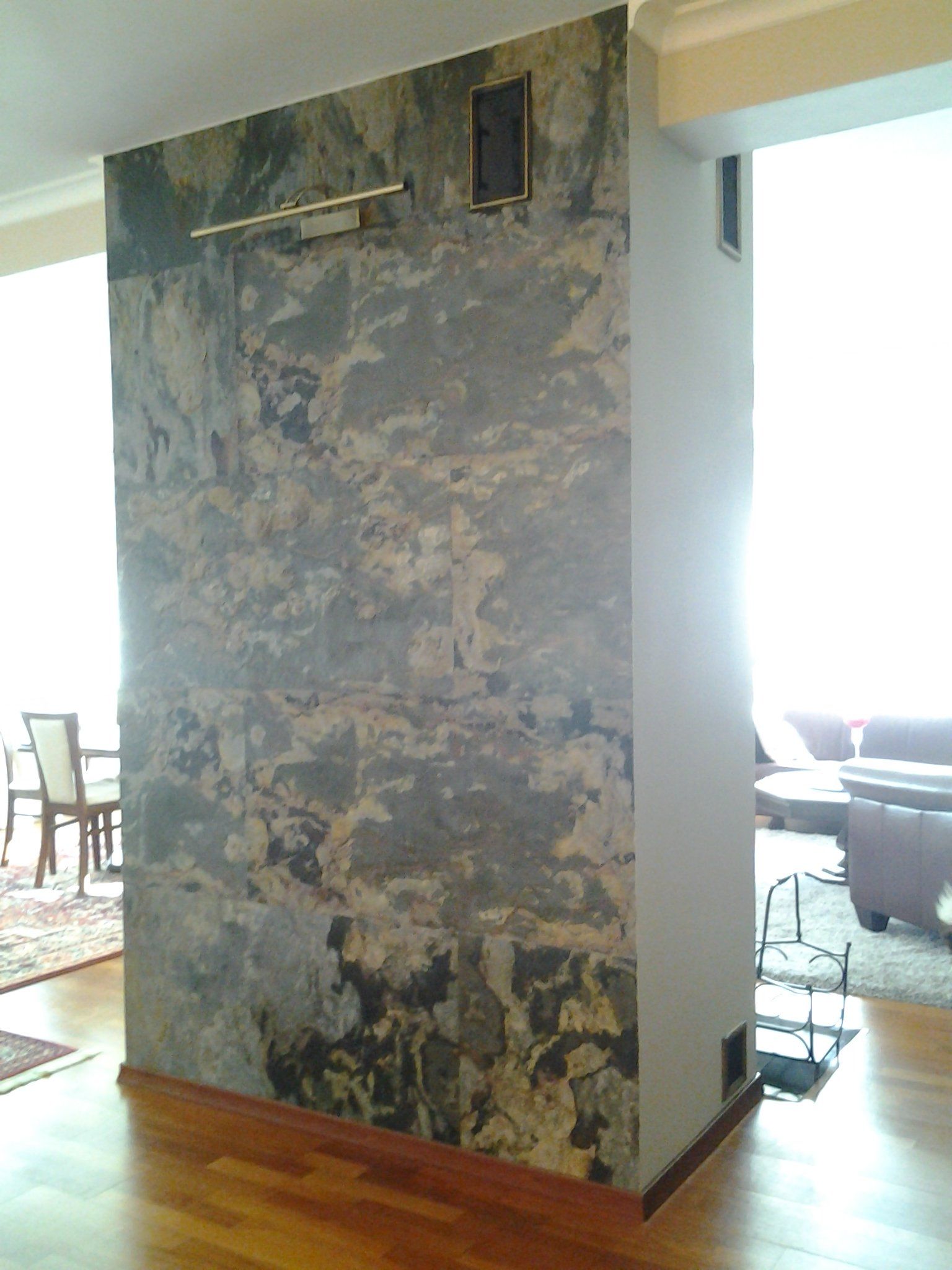 Stone-clad feature wall in a room with hardwood floors. A light fixture and vents are visible. Sunlight streams in from the right.