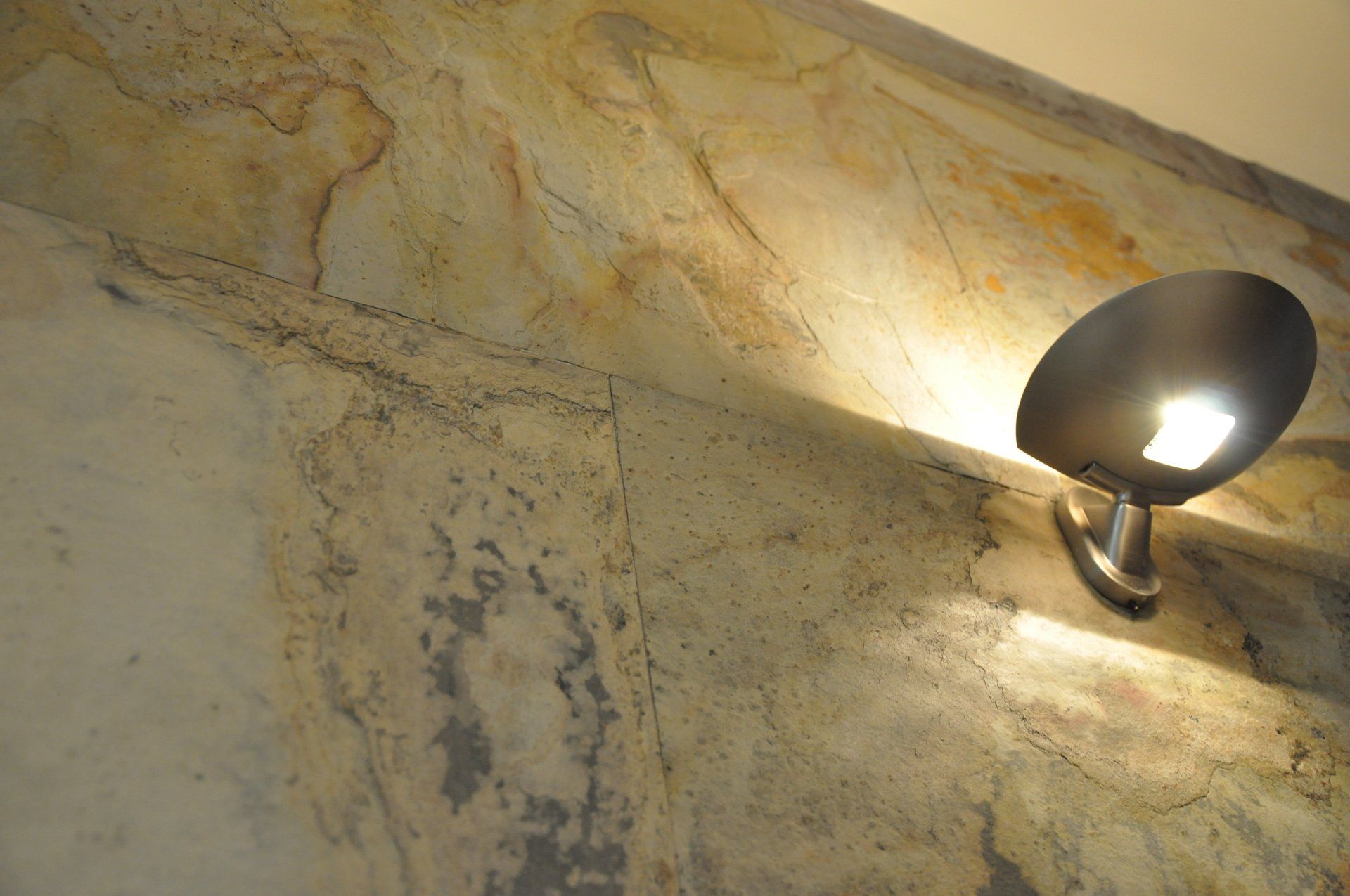 Wall with abstract patterns, illuminated by a spotlight.  Faded colors, light reflecting off the surface.