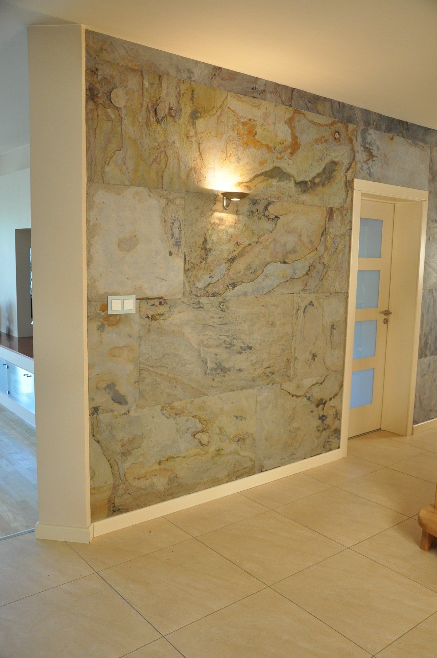 Wall with textured stone finish, recessed lighting, and a door. Pale floor and white trim.