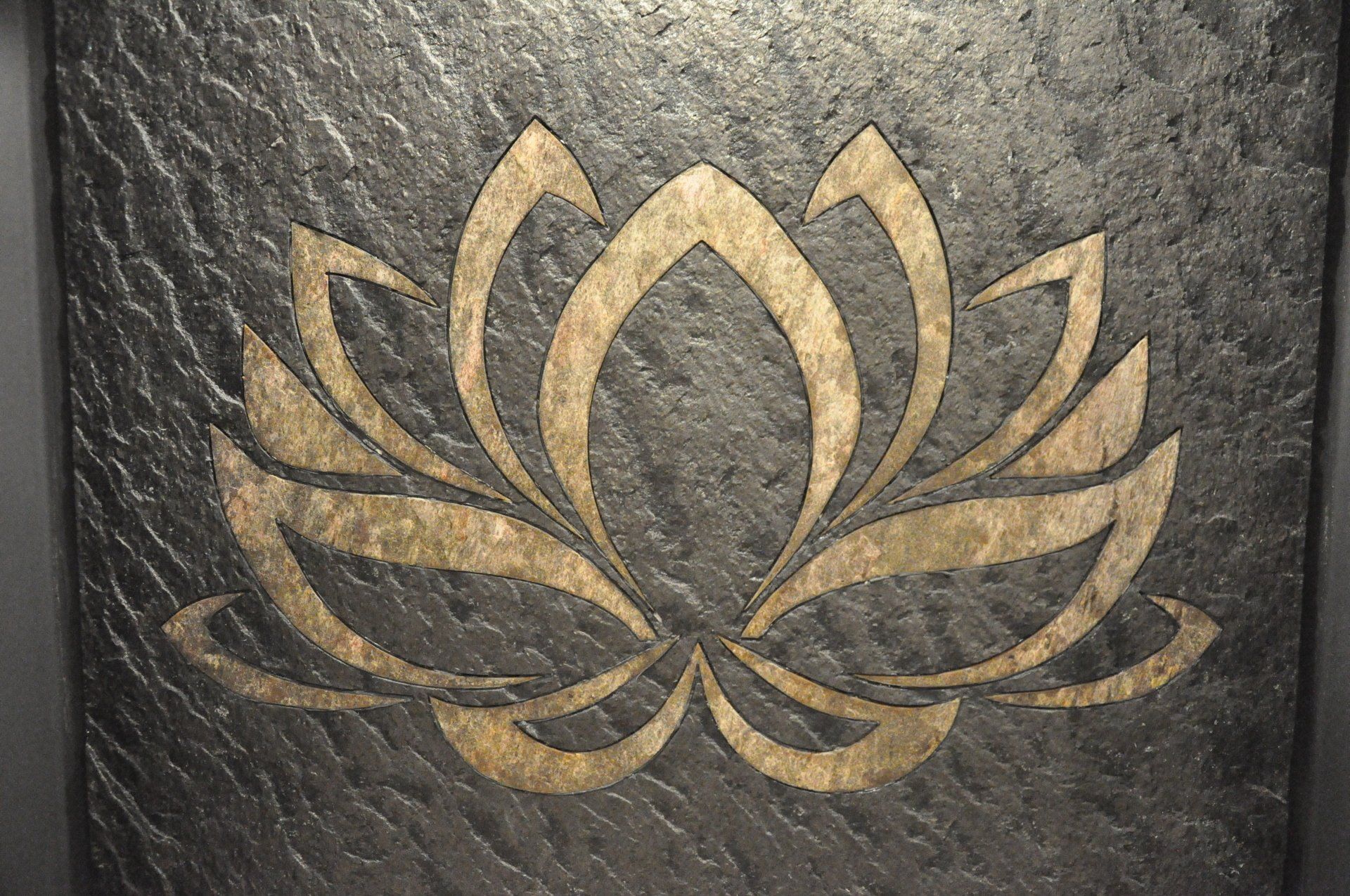 Gold lotus flower etched on a textured gray stone.