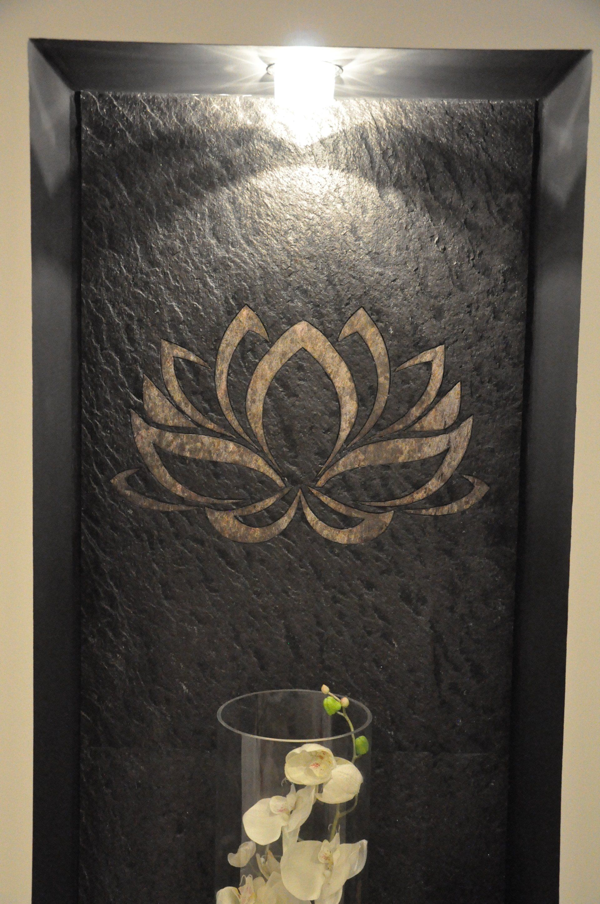 Black wall niche with a lotus flower design lit by a spotlight, featuring a glass vase with white flowers.