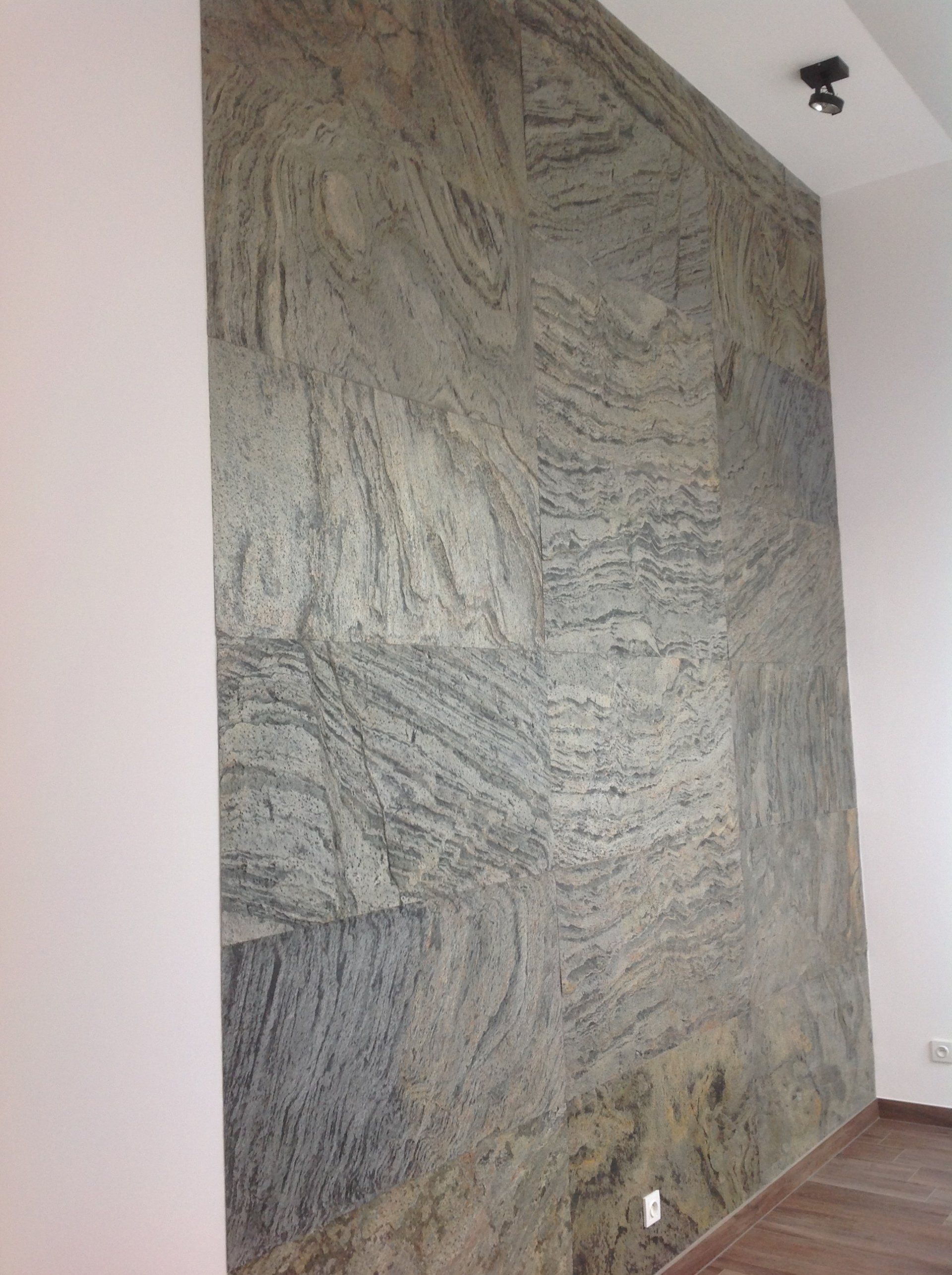 Stone-tiled accent wall with gray and cream swirling patterns. In a room with white walls and a wooden floor.