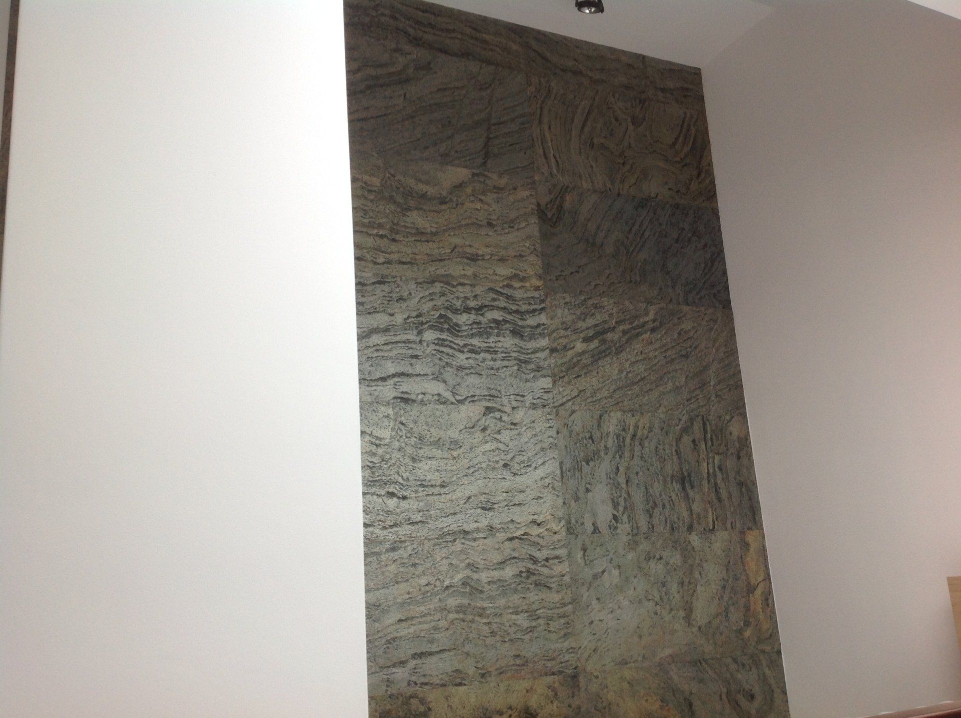 Stone-tiled wall section between two white walls, natural stone texture in shades of gray, beige, and brown.