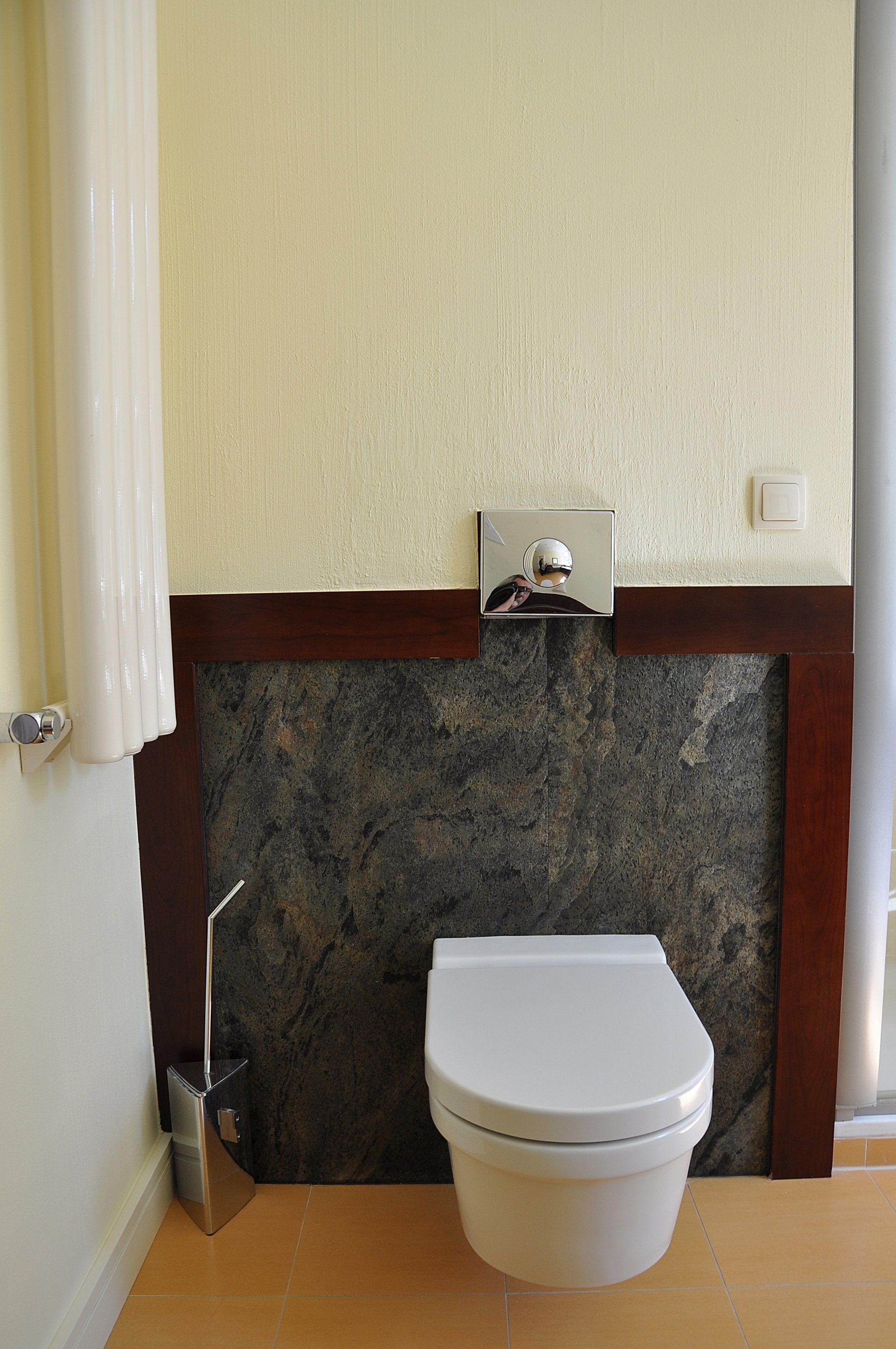 Toilet in a bathroom with dark stone accent wall, cream walls, and wood trim.