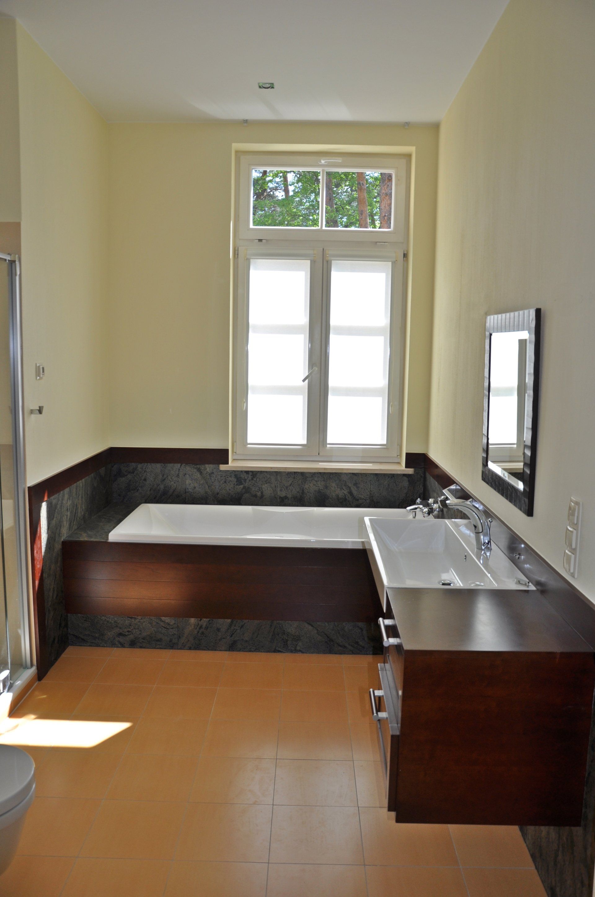 Bathroom with built-in tub under a window, dark wood vanity, and beige walls.