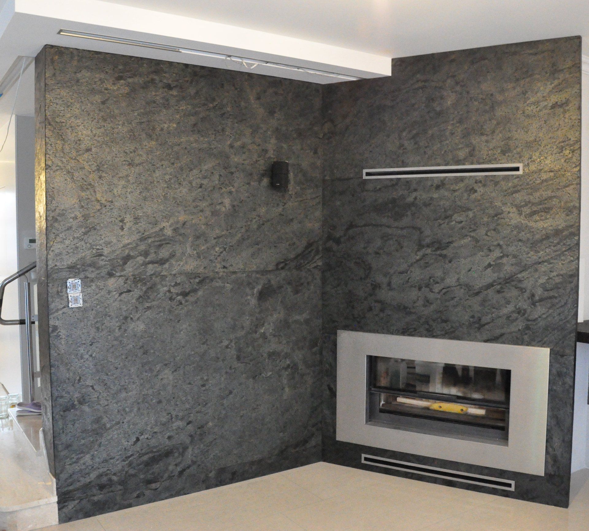 Corner of a room with dark gray stone wall surrounding a fireplace with a silver frame.