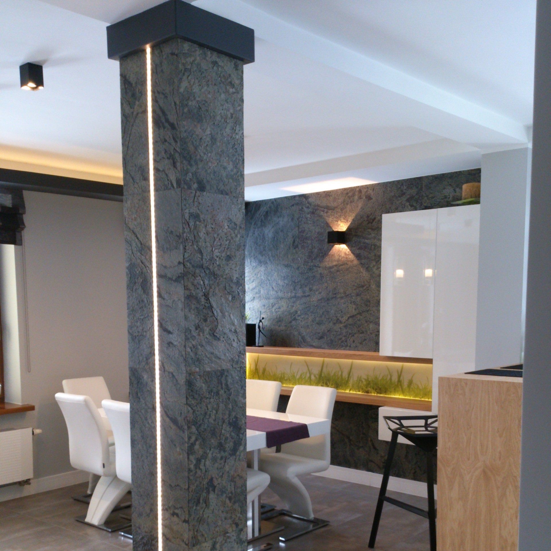 Dining room with gray stone column, recessed lighting, white chairs, dark accent wall.