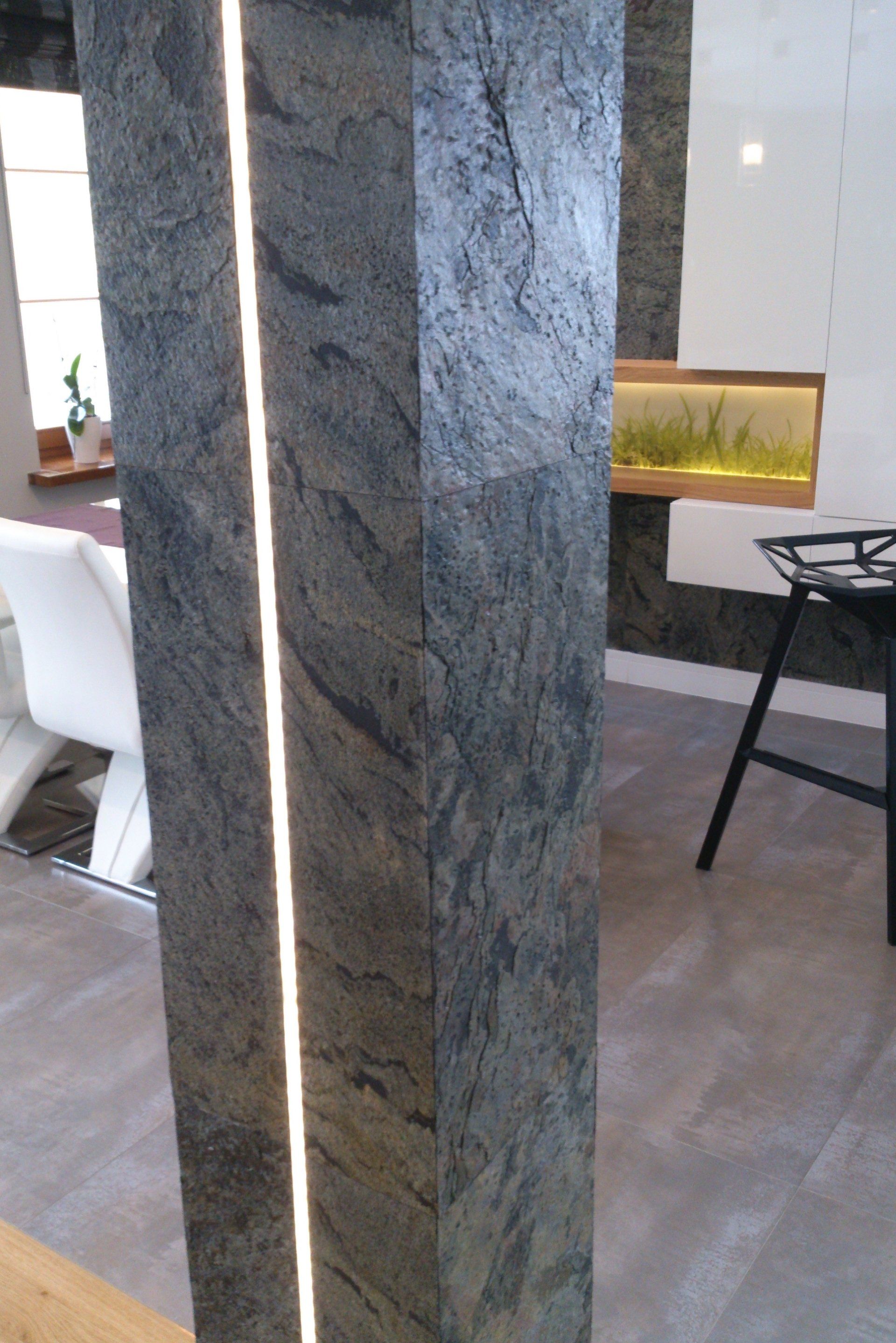 Gray stone pillar with vertical light strip, in a modern interior; in the background, there's an aquarium and a black stool.