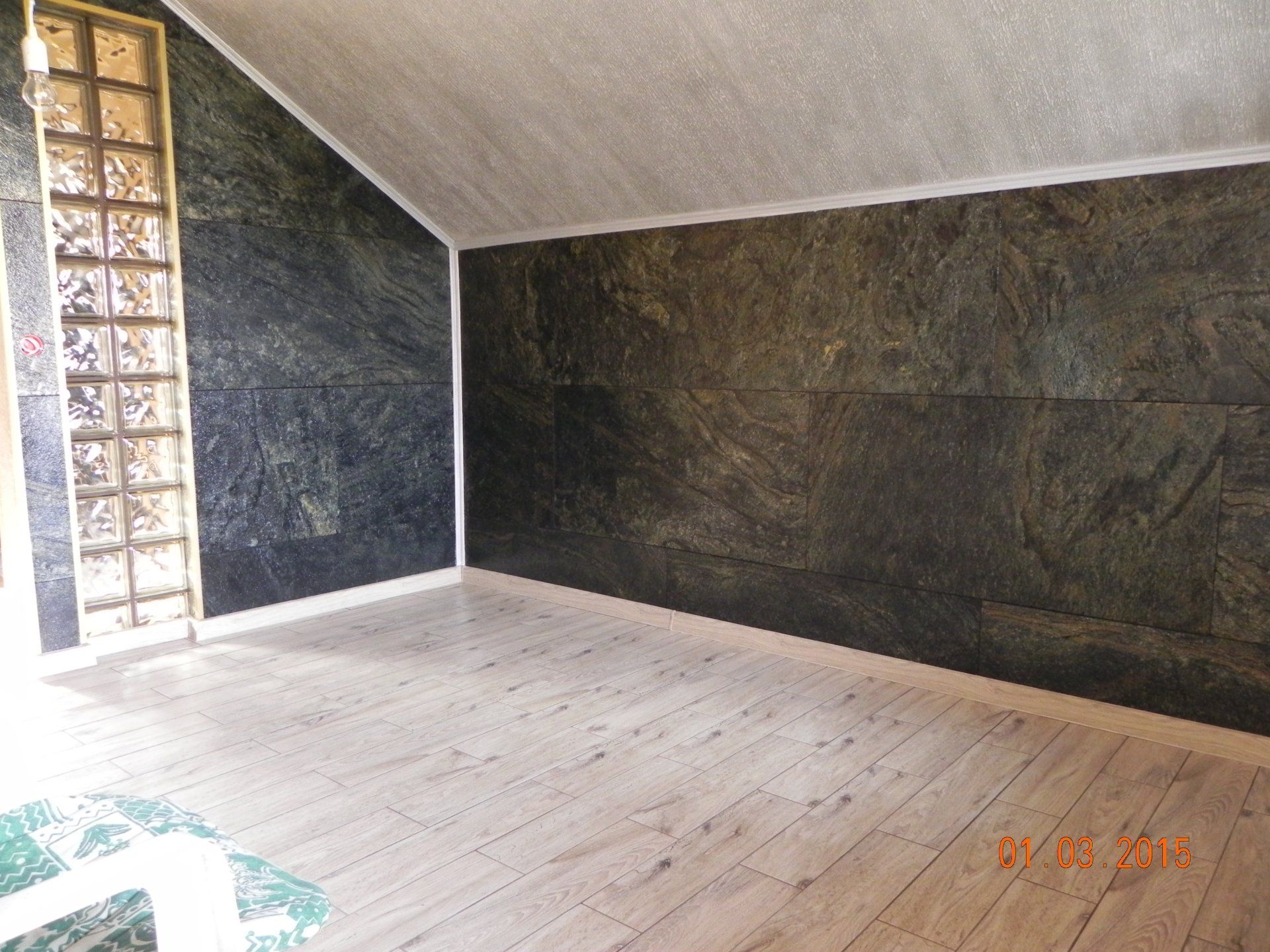 Empty room with dark green stone walls, light floor, and glass block window.