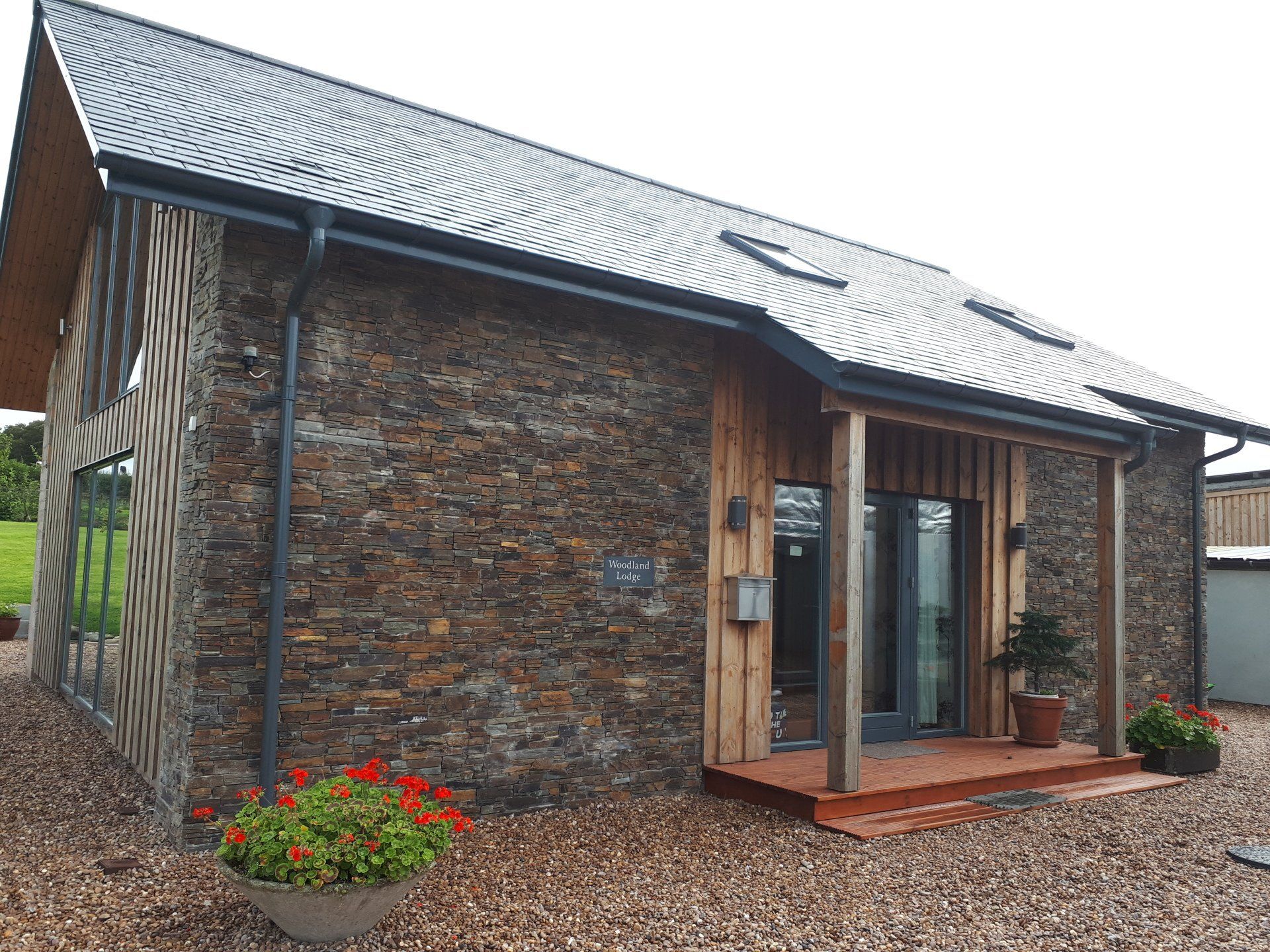Stone and wood-clad modern building with a slate roof, a porch, and gravel landscaping.