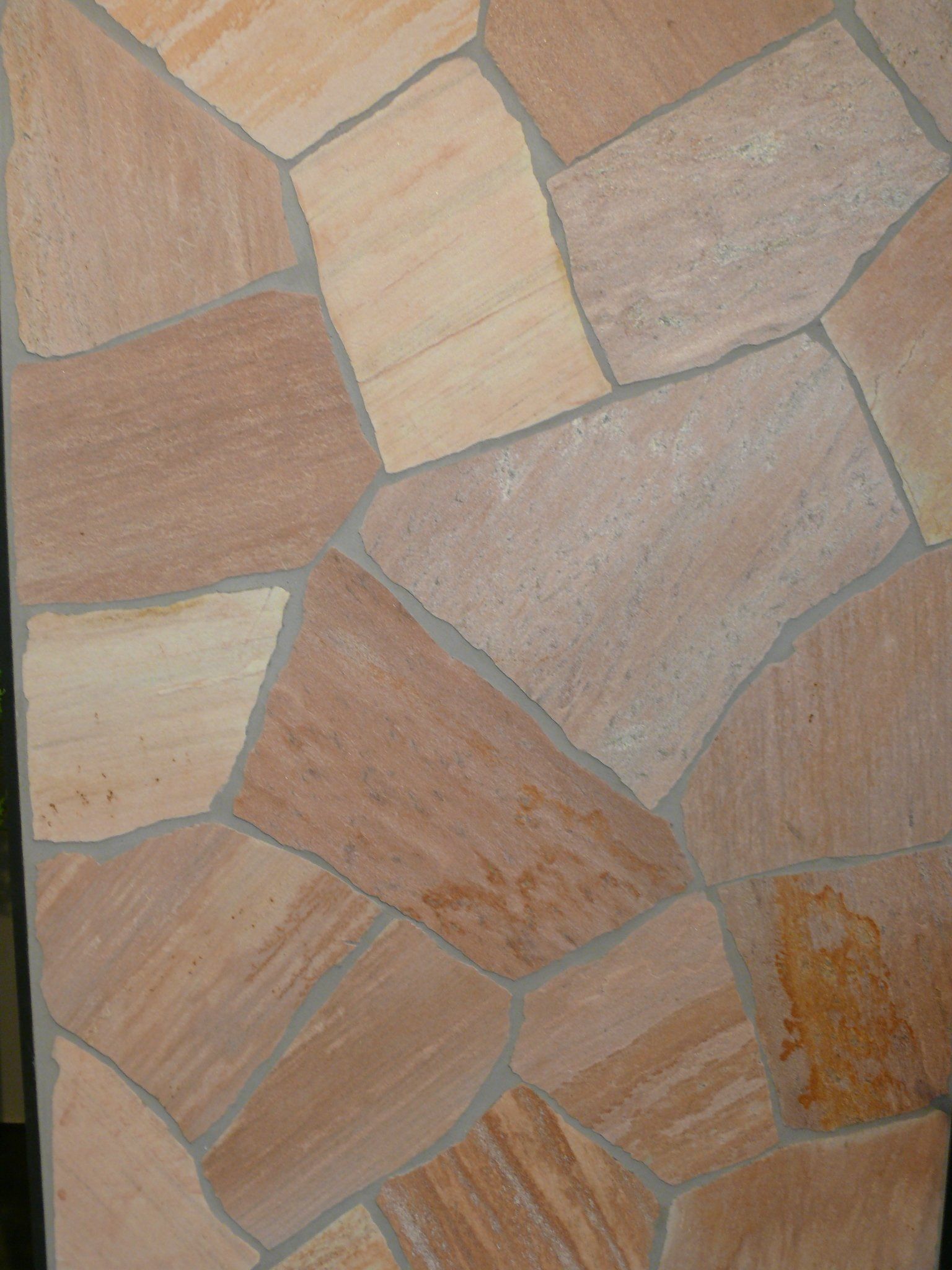 Close-up of a wall made of irregularly shaped, earth-toned sandstone tiles with gray grout.