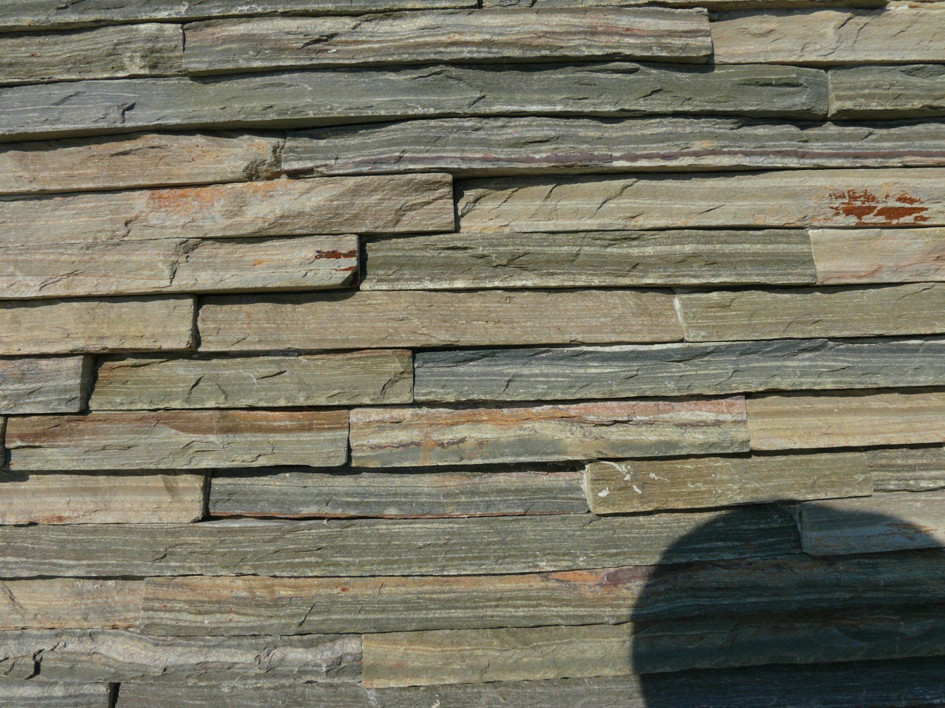 Stacked stone wall with varying shades of gray, green, and tan.