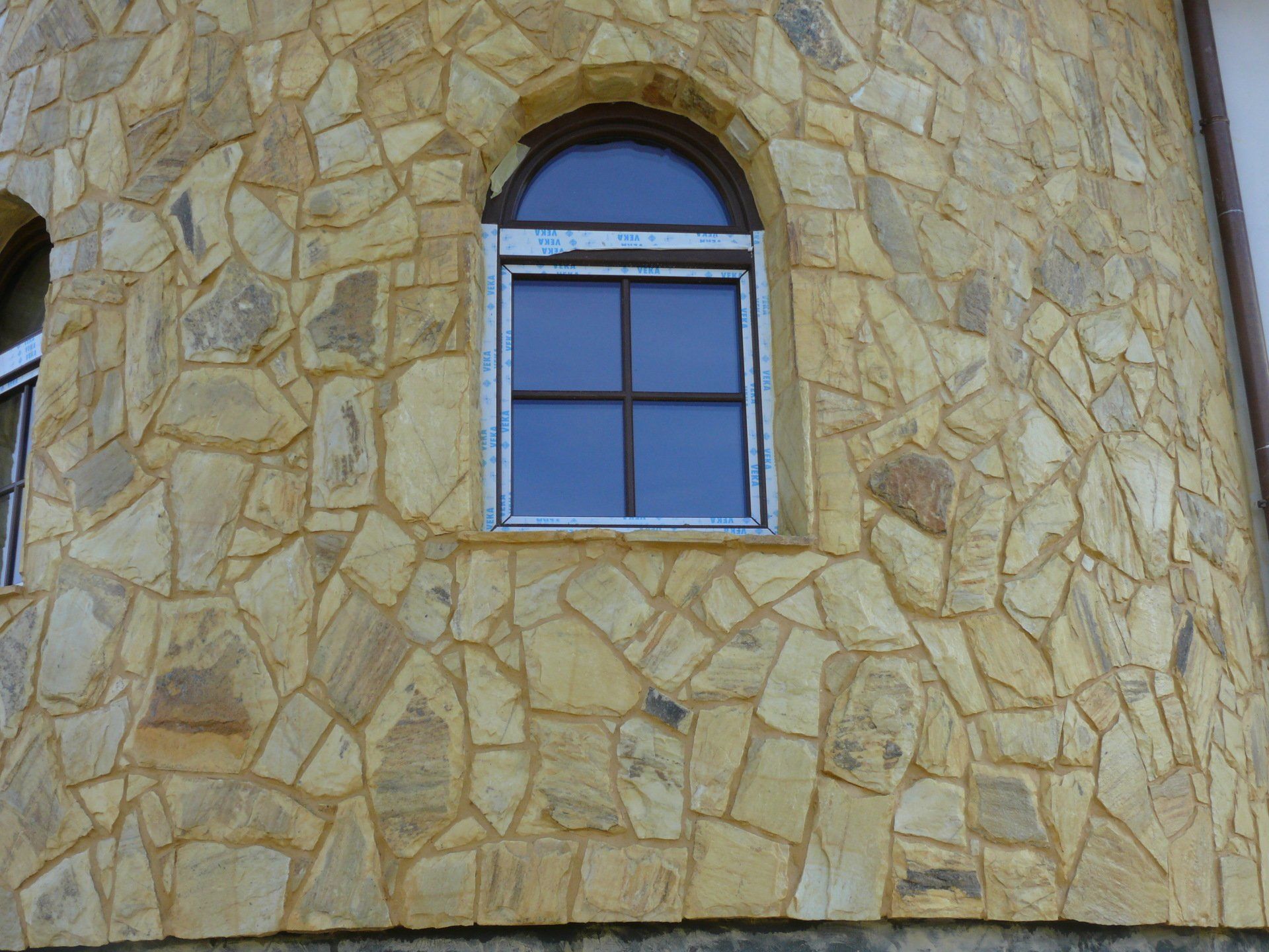 Window with arched top set into a yellow stone exterior of a building.