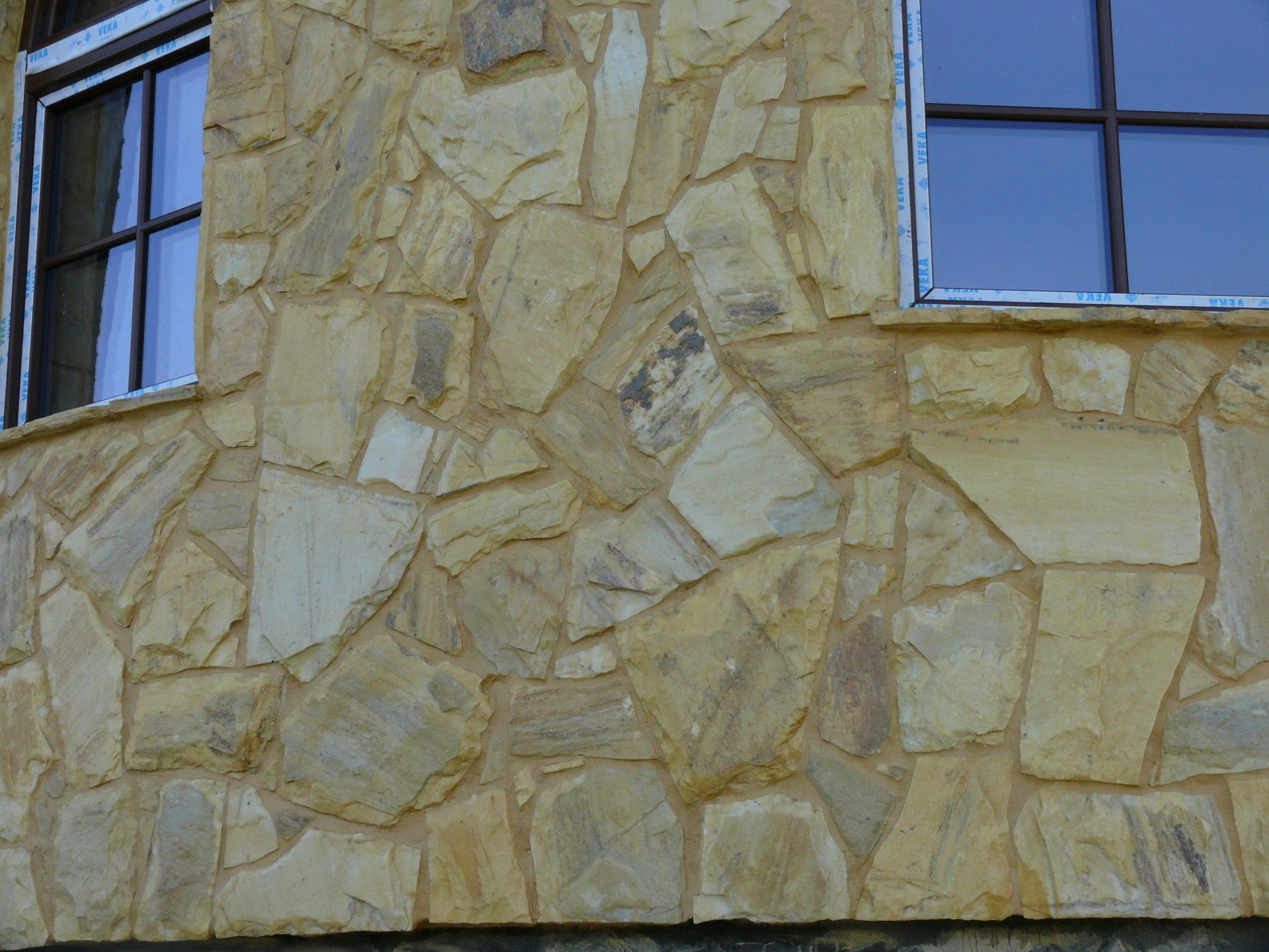 Exterior stone wall with two windows; tan and beige stones with brown window frames.