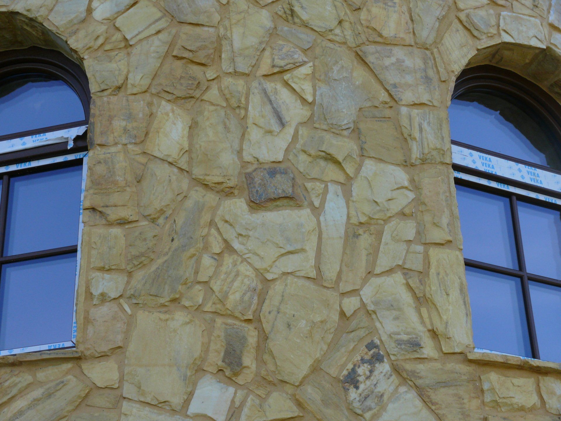 Two arched windows with dark frames set in a textured, light brown stone wall.