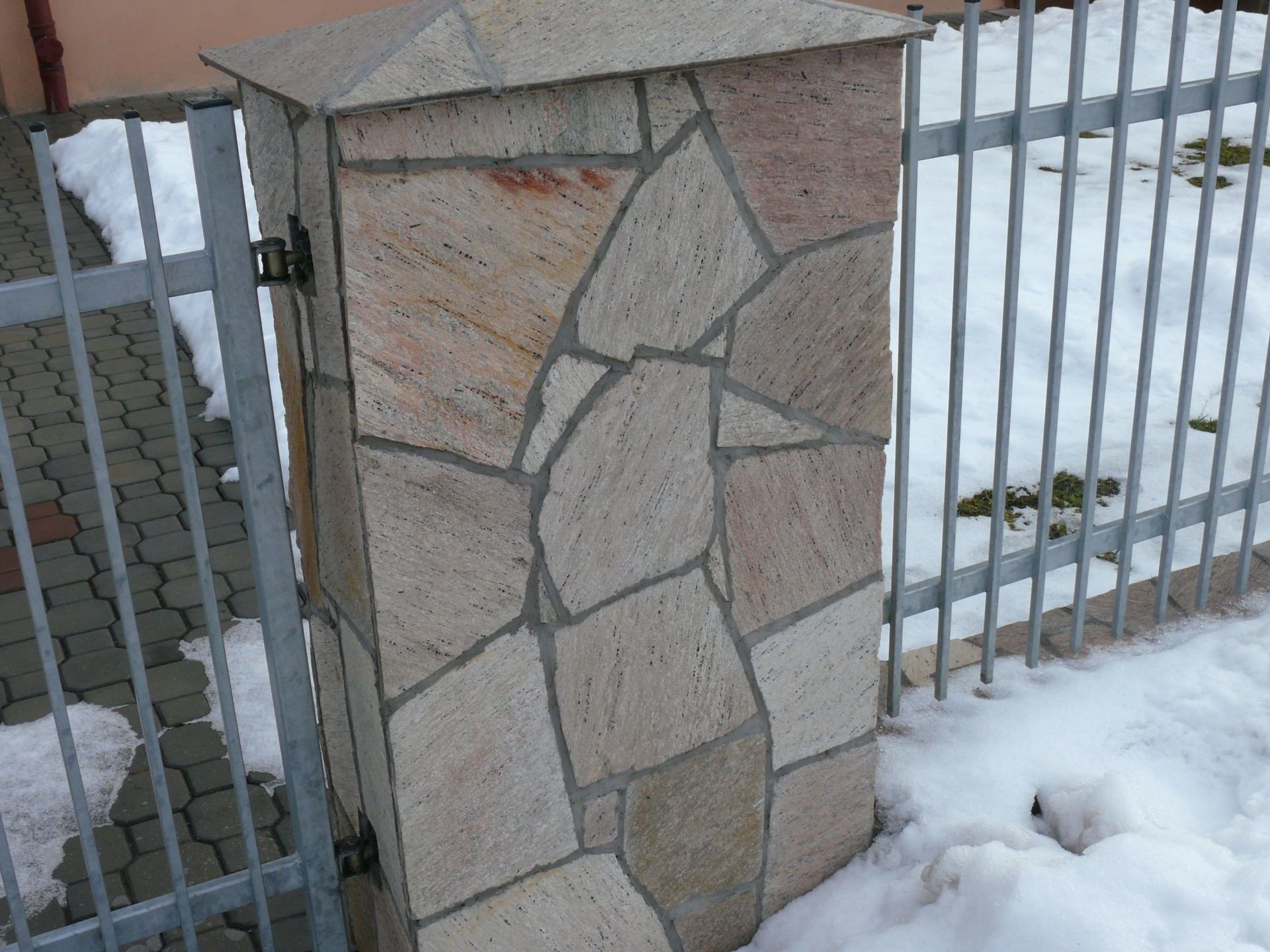 Stone pillar with a metal gate and snow on the ground.