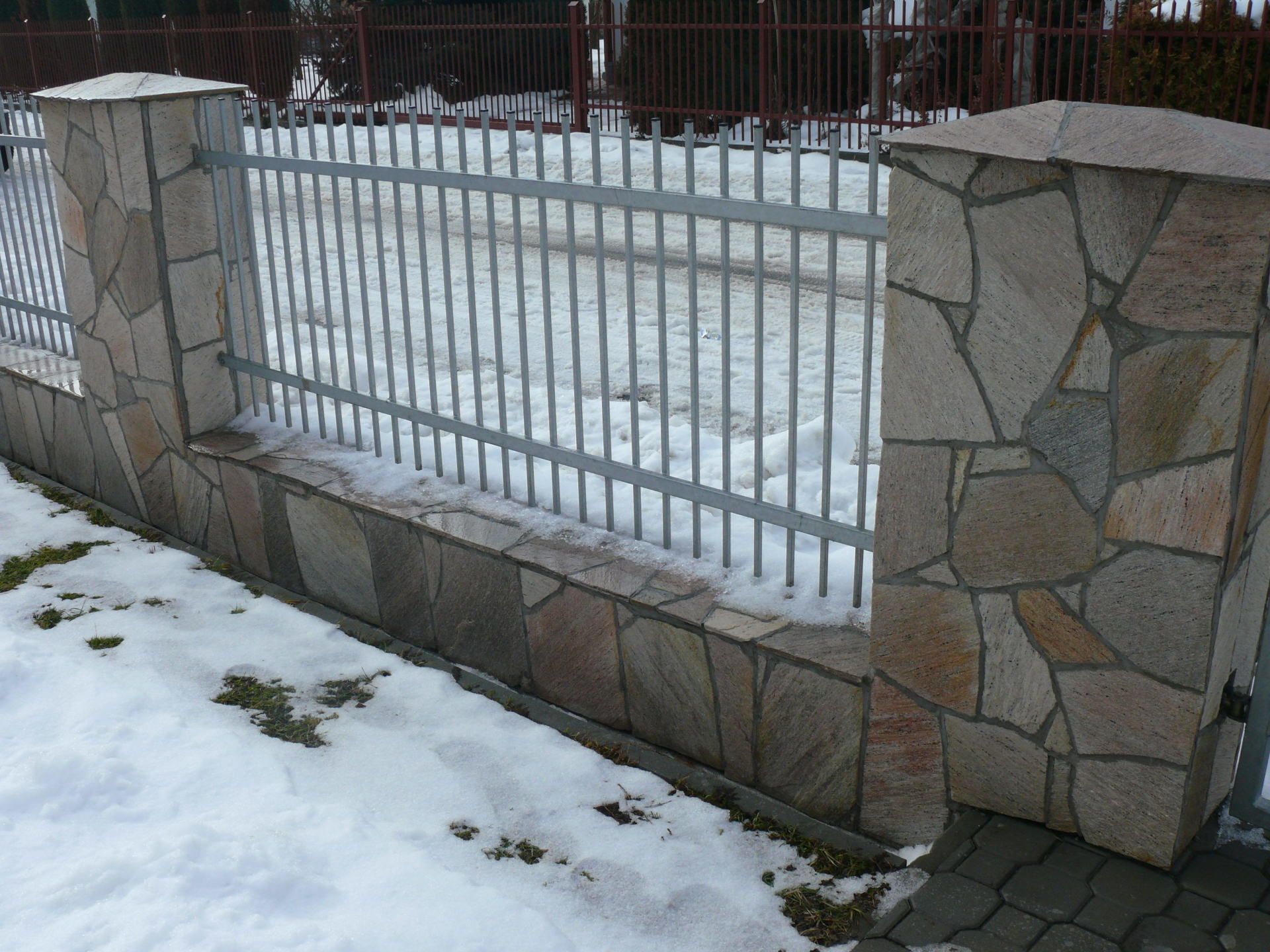 Stone and iron fence on snowy ground.