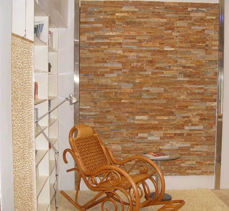Wicker rocking chair in front of a brick wall, next to bookshelves and a small table.
