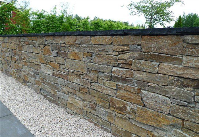 Stone wall with varying shades of brown and gray stones, topped with a dark border, with gravel at its base.