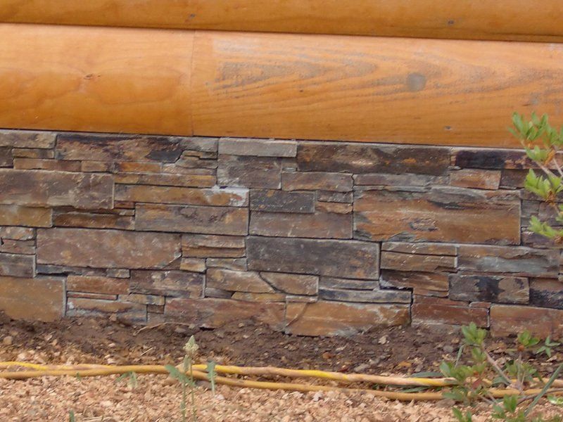 Stone veneer base of a wooden cabin. Earth-toned stones with natural variation. Logs are light brown.