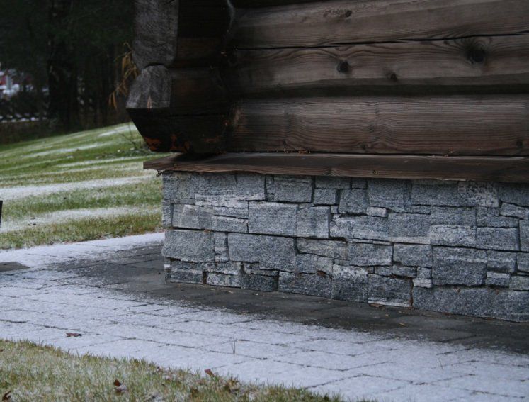 Corner of log cabin with stone foundation and snow-covered ground.