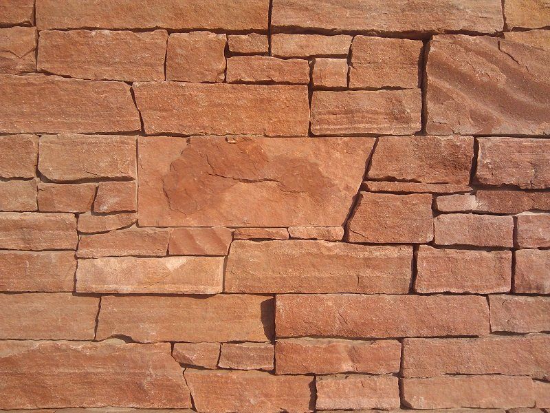 Reddish-brown stone brick wall, textured, with varying sized rectangular blocks.