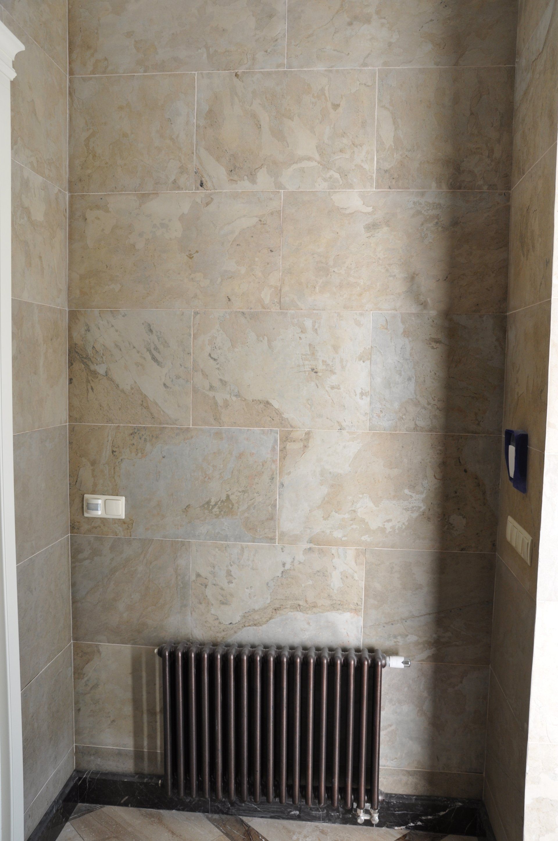 Stone-tiled wall with a radiator at the bottom. A white outlet and blue switch plate are visible.