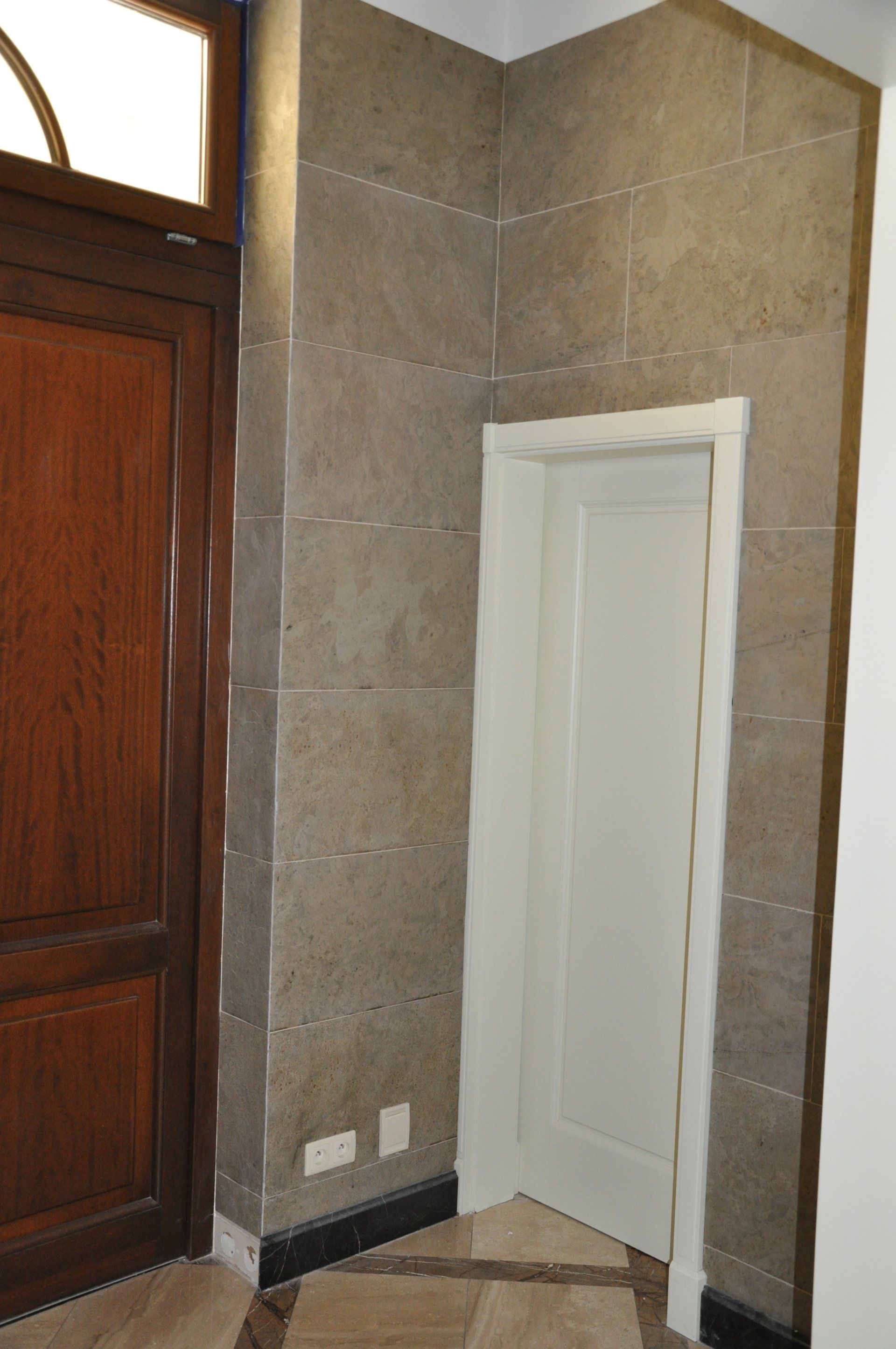 Brown wooden door next to a tiled wall with a white door.