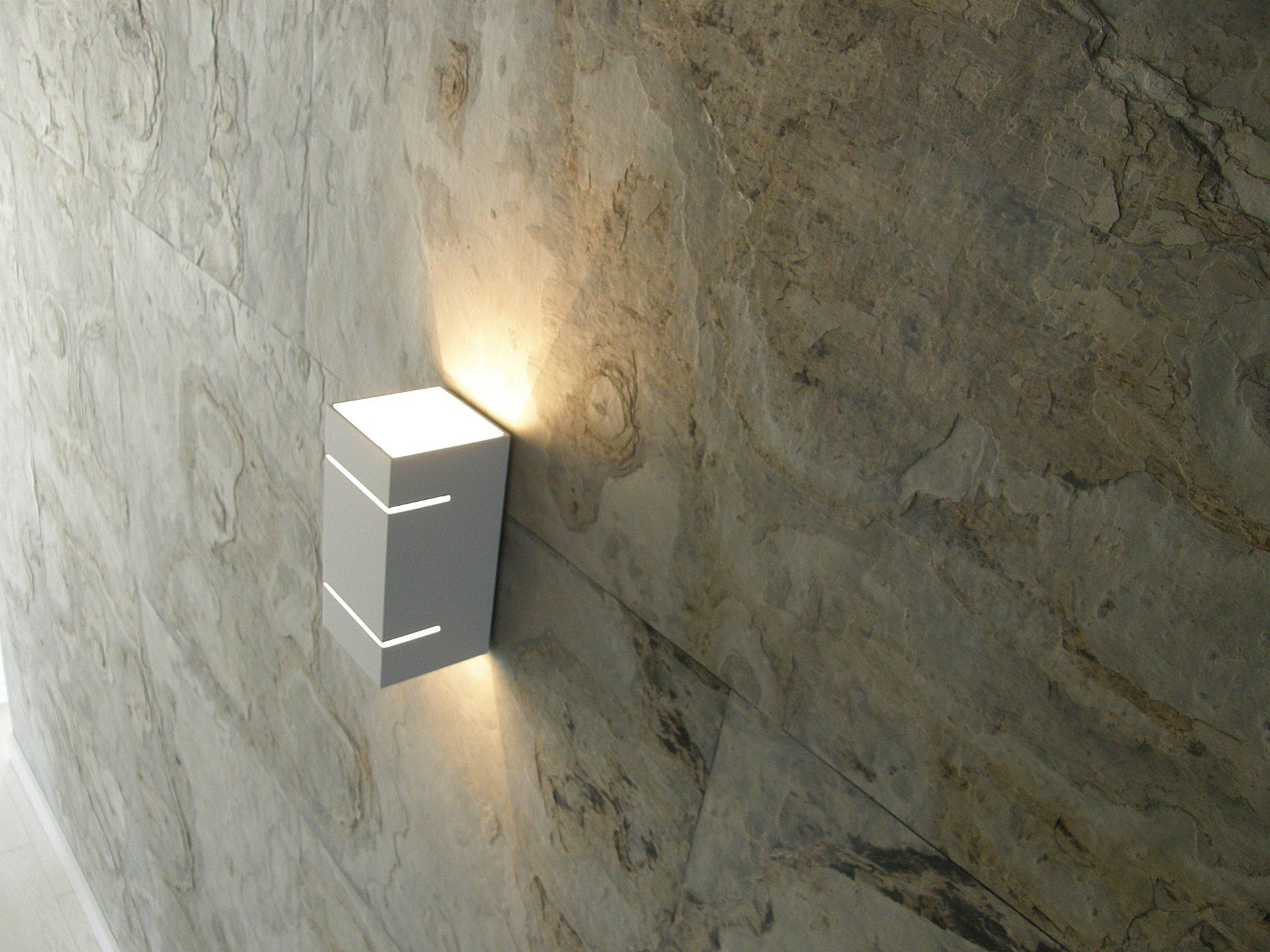 White rectangular wall light on a textured stone wall, emitting light downwards and upwards.