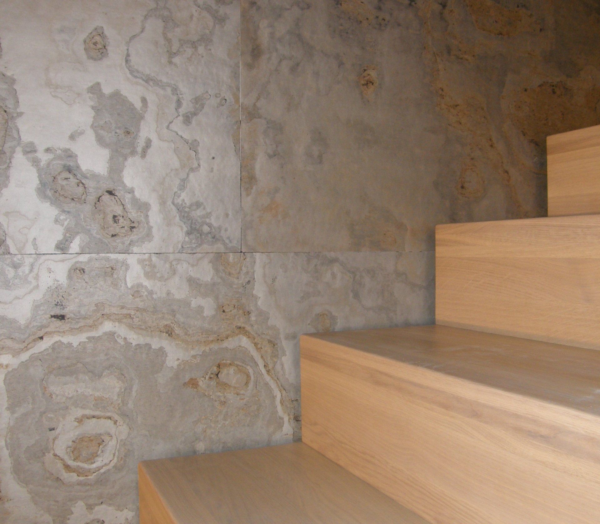 Wooden staircase next to a wall with patterned, marble-like stone panels.