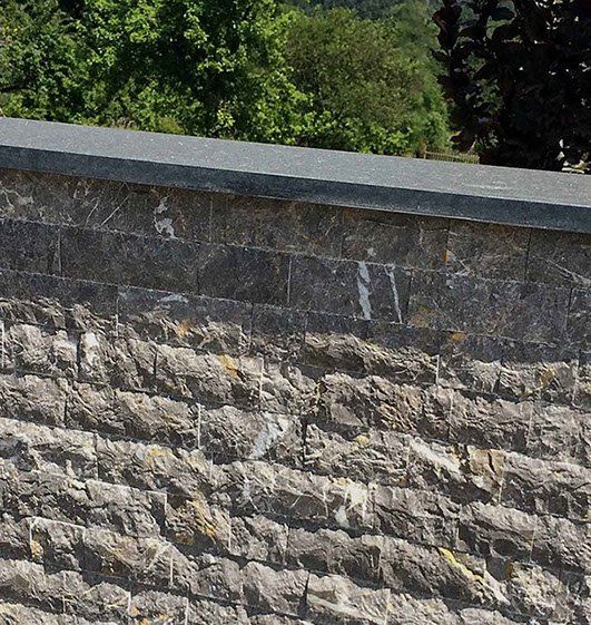Stone wall with dark gray cap; green trees in the background.