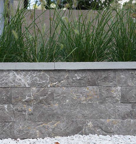Stone wall with grass plants on top, white pebbles at the bottom.