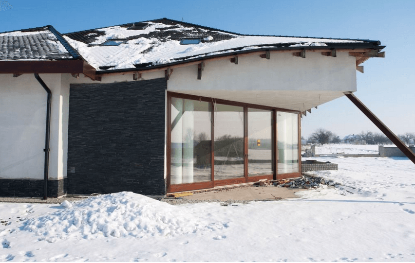 House exterior with snow, large windows, wooden frame, and dark slate wall.
