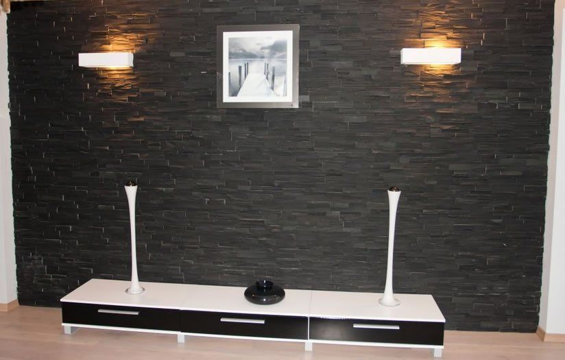 Black stone wall with white and black entertainment center, artwork, and sconce lighting.