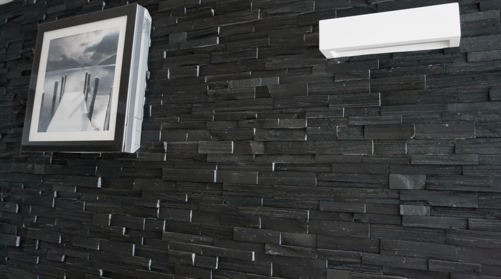 Black brick wall with a framed photo and a white air conditioner unit.