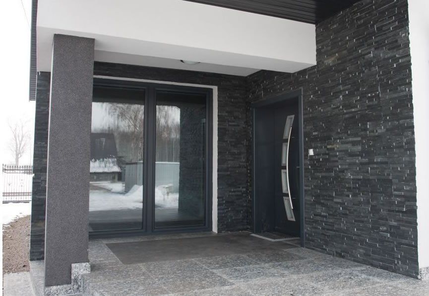 Exterior of a modern house with a dark gray door and stone-covered wall.