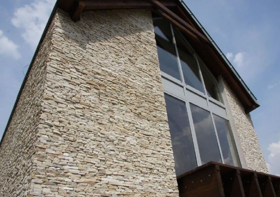 Stone-clad building with large windows and a wooden beam roof against a blue sky.
