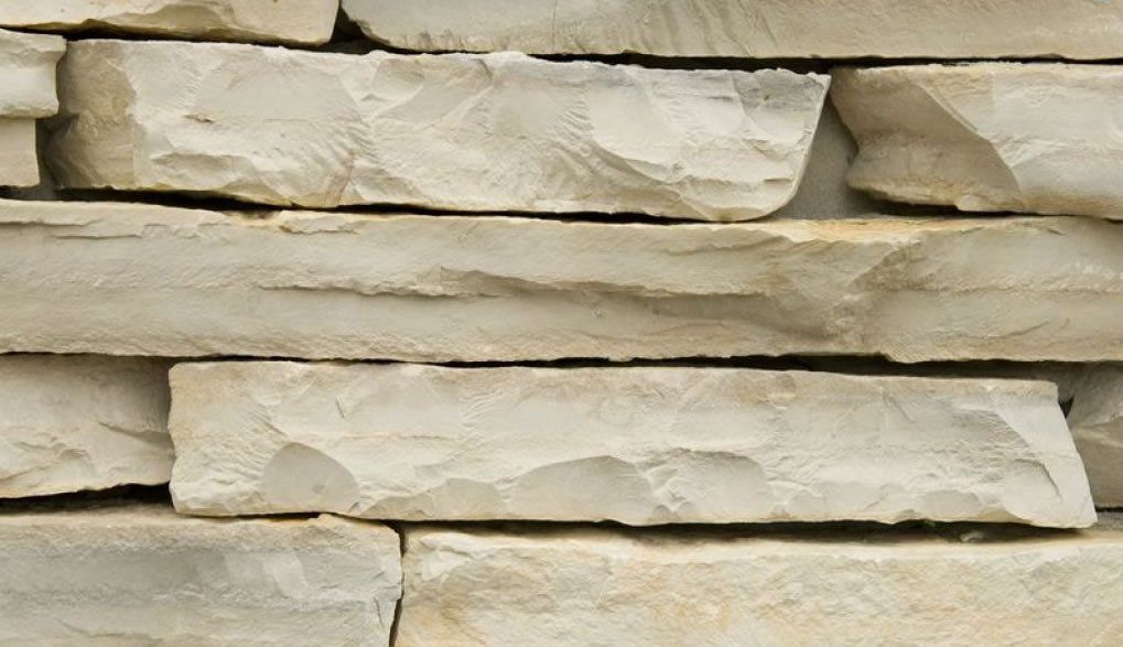 Close-up of a light beige stone brick wall with rough-cut edges.