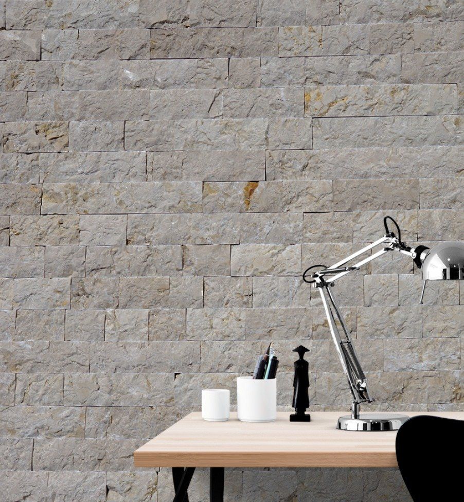Desk with lamp, pens, and cup against a textured gray stone wall.
