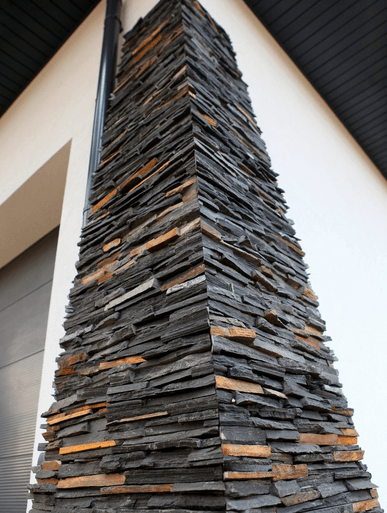 Corner of a building with layered, dark gray and brown stone cladding.