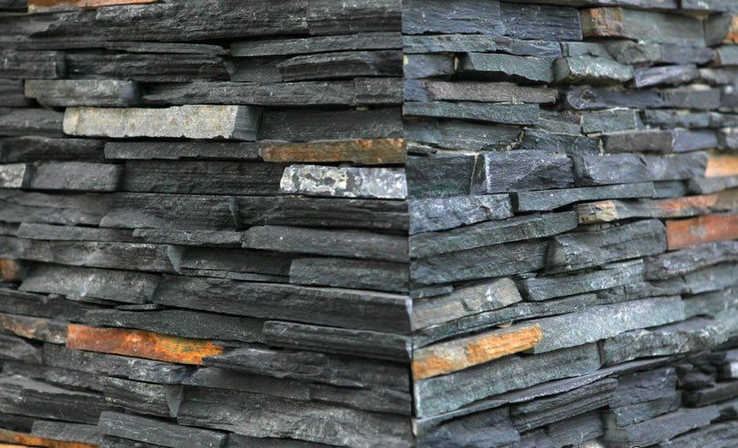 Stone wall corner, layered slate in gray, black, orange, and tan.