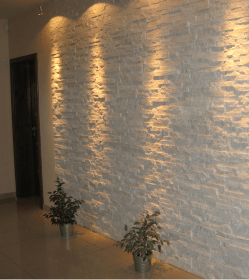 White textured wall with spotlights, two small plants in metallic pots, and a dark doorway.