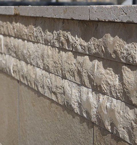 Stone wall with rough-hewn horizontal bands and smooth top edge; neutral beige and gray tones.