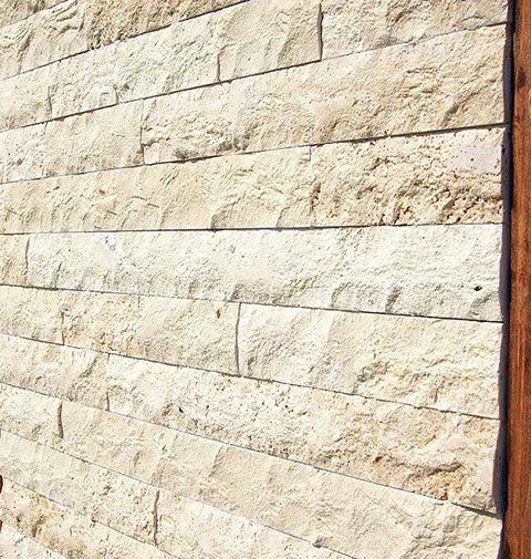 Stone wall with rectangular, textured, light beige bricks.