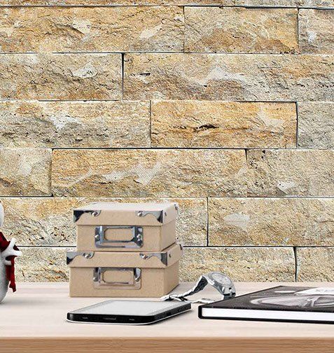Stacked beige boxes, electronic devices, and a book on a wooden surface in front of a stone wall.