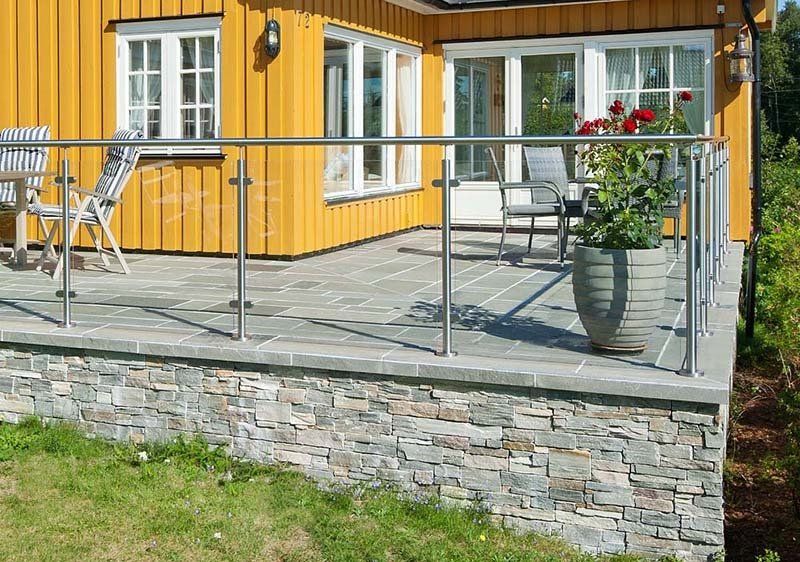 Yellow house with stone patio, glass railing, and potted roses.